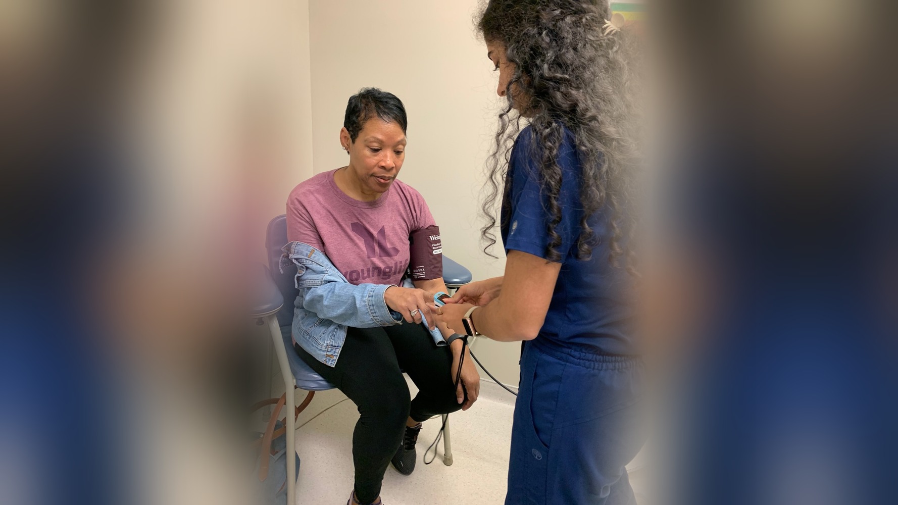 A Mercy volunteer in navy scrubs placing a pulse oximeter on a seated patient's finger