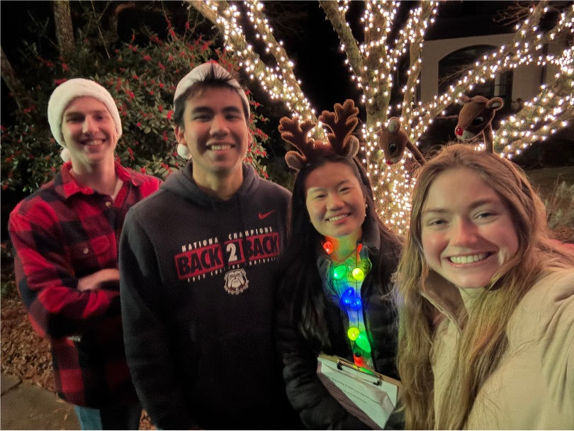 Four friends wearing reindeer antlers and a light-up necklace beneath Christmas lights