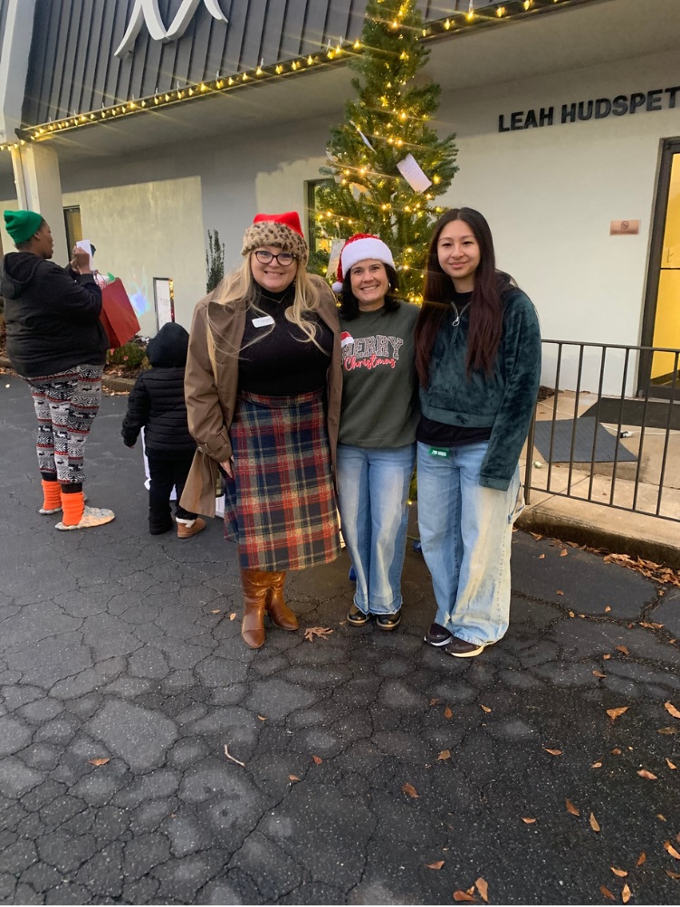 Three volunteers smiling beside Mercy’s Christmas tree