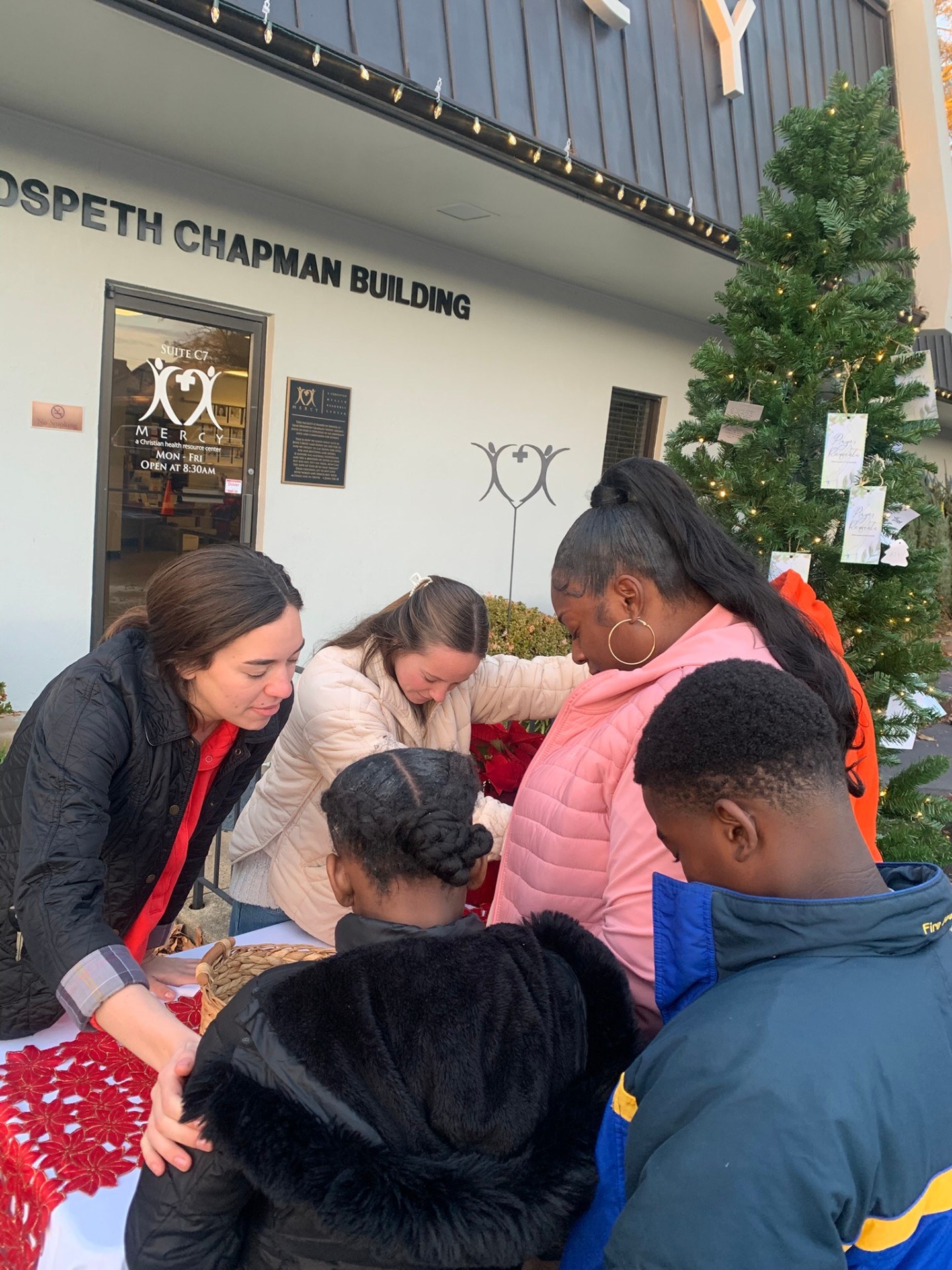 Mercy volunteers praying with a family beside the Christmas tree