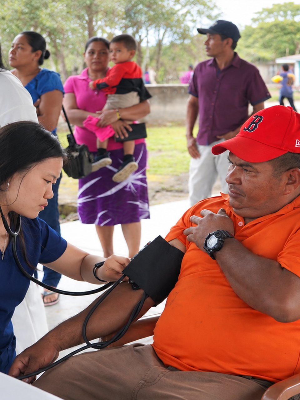 A Mercy Health Center clinician checking a seated patient's blood pressure at an outdoor community clinic