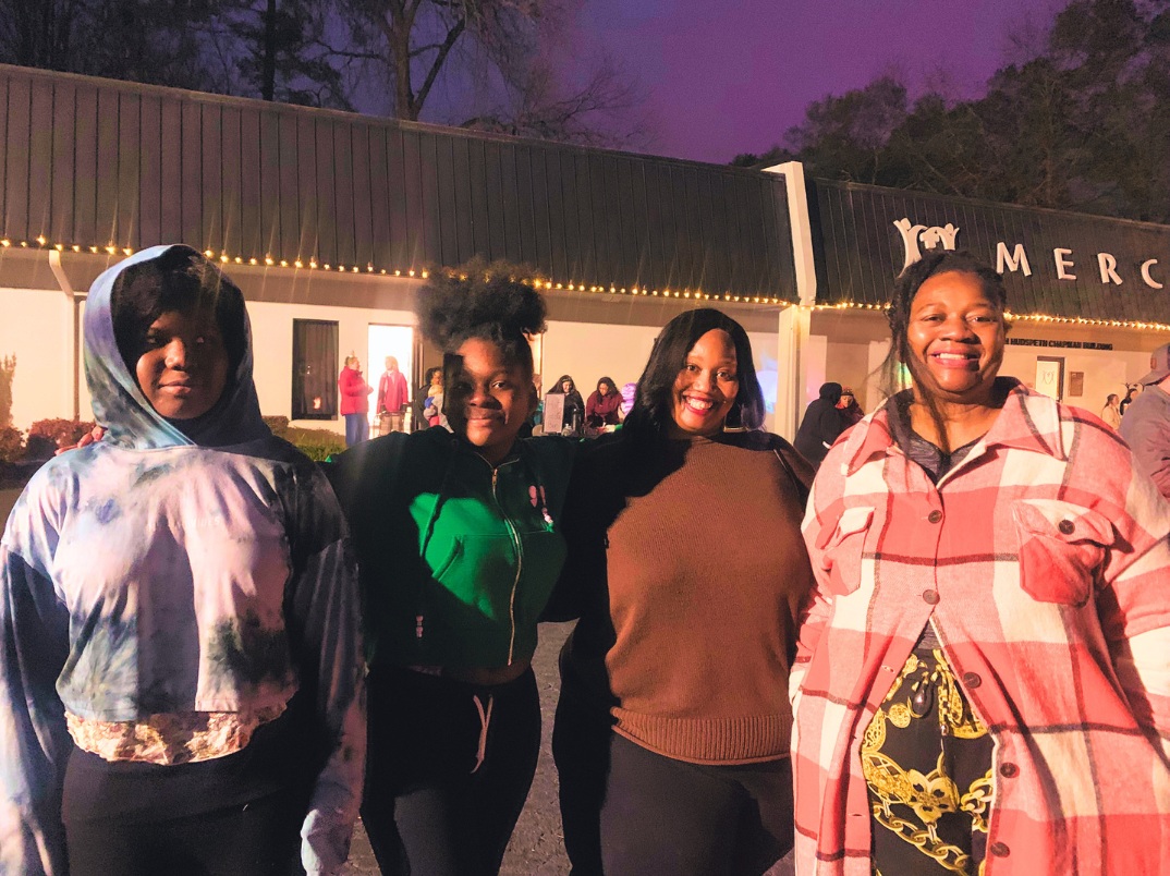 Four guests celebrating Christmas outside Mercy beneath the clinic’s string lights