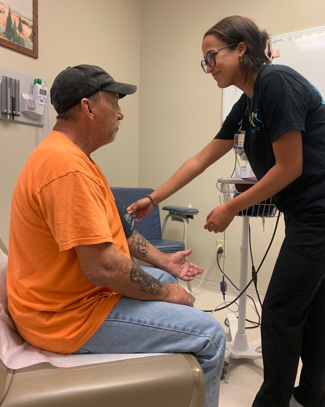 A Mercy healthcare provider checks a seated patient’s blood pressure in an exam room.