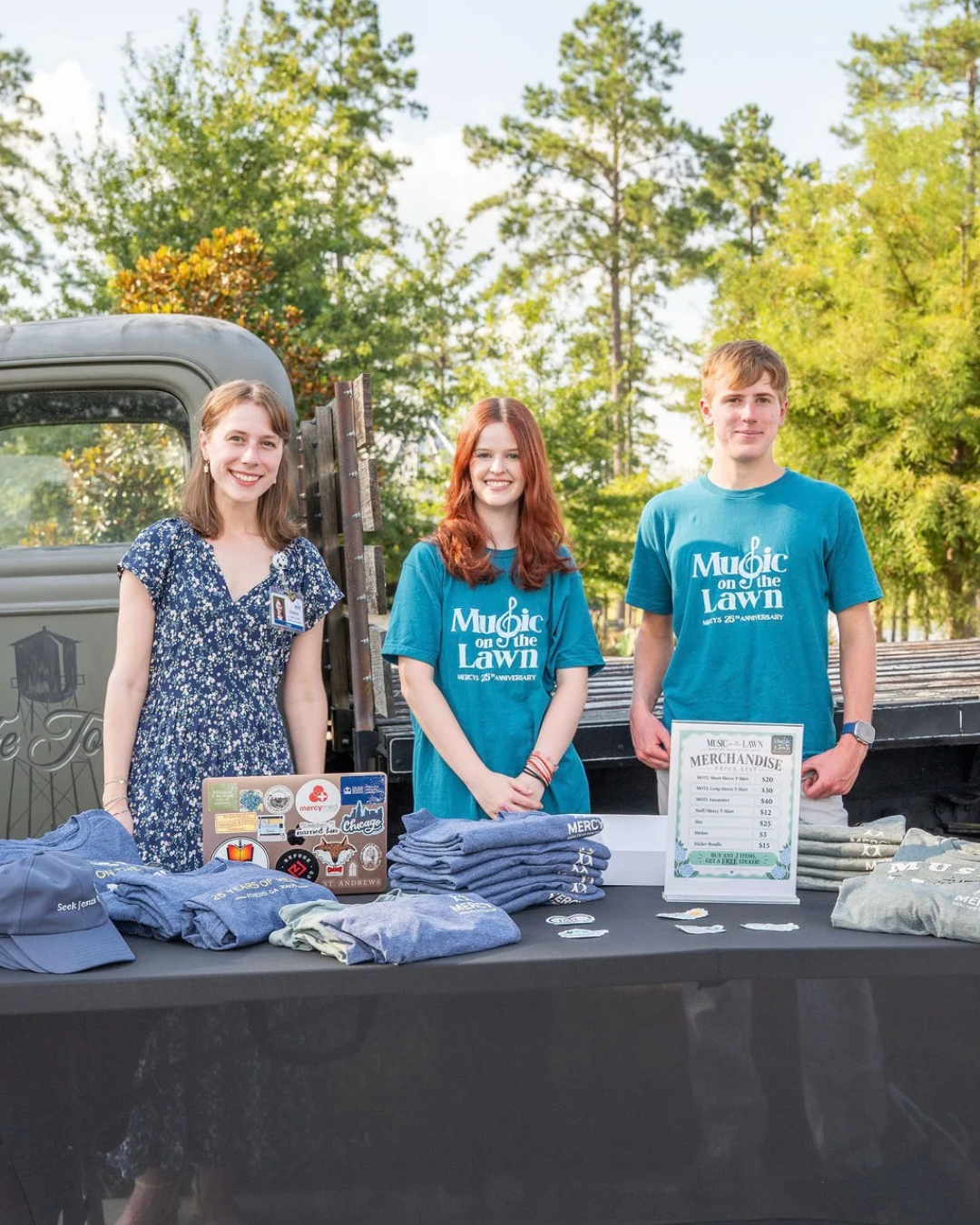 Three Mercy volunteers at the Music on the Lawn merchandise table