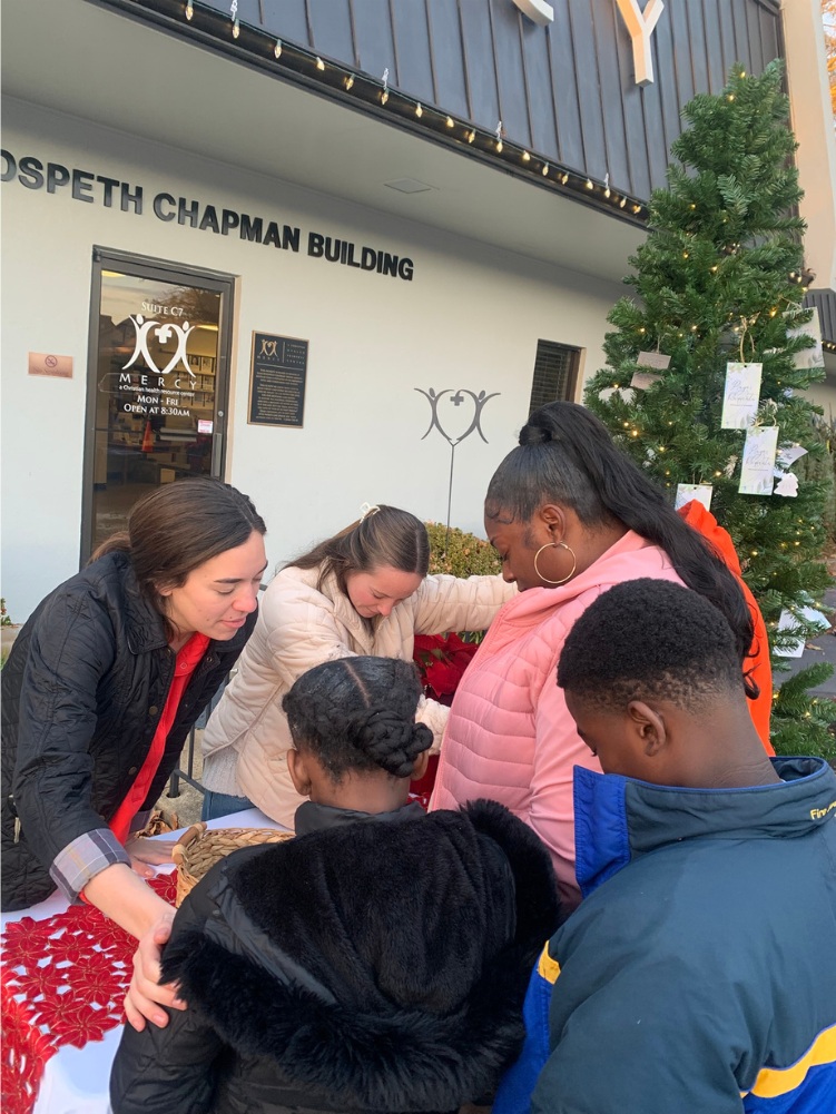 Volunteers and families gathered around a table beside Mercy’s Christmas tree